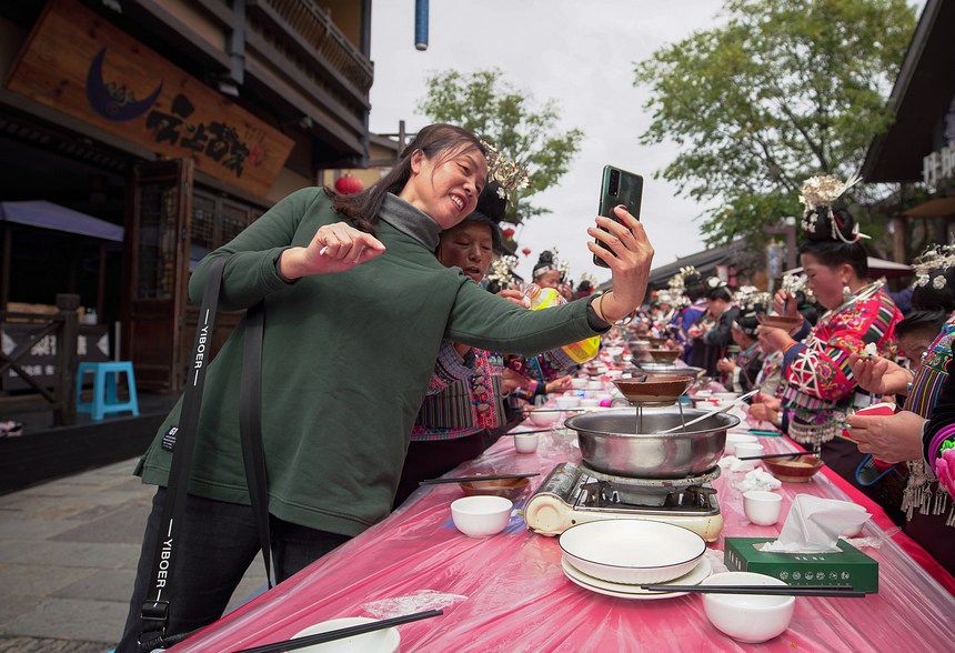 10月31日，游客在丹寨縣萬達小鎮長桌宴上與苗族同胞合影。
