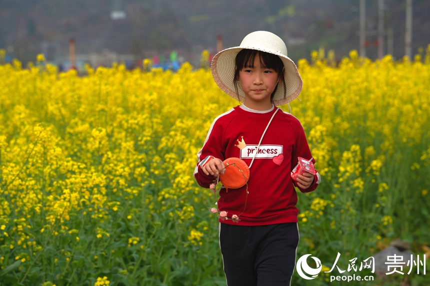 游客站在田坎上與盛放的油菜花合影。人民網 陽茜攝