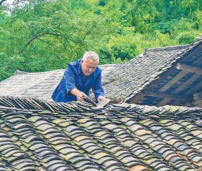 圖為萬明春在撿瓦，修補漏雨的地方。蘇 濱 涂 敏攝影報道