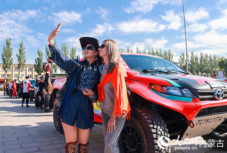 8月22日，外國游客在中國庫布齊沙漠越野賽暨中國汽車越野拉力錦標(biāo)賽杭錦旗分站賽開幕式活動現(xiàn)場打卡留影。丁根厚攝