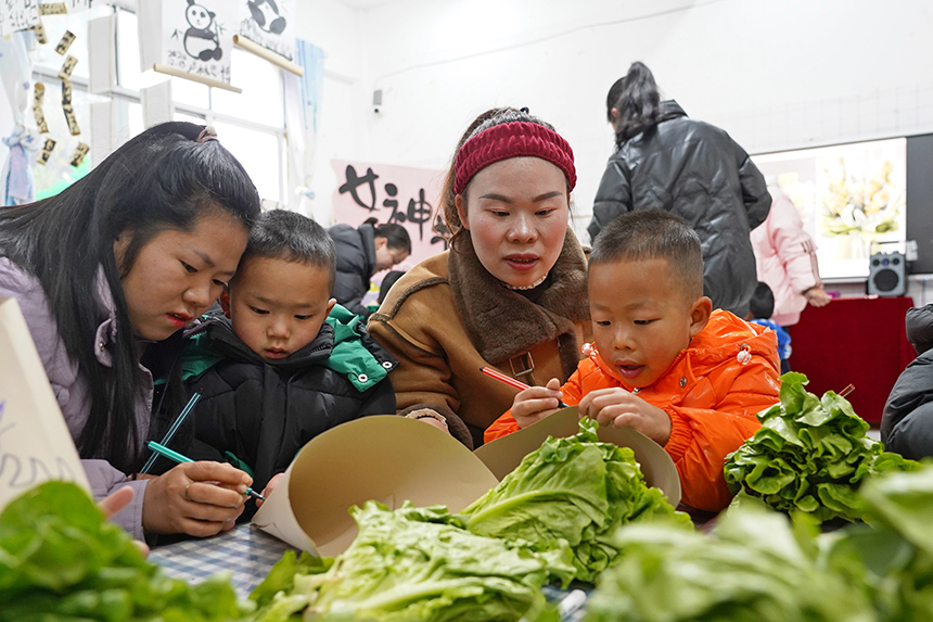 2025年3月6日,貴州省畢節市納雍縣龍場鎮中心幼兒園“溫情三八·感恩有您”活動現場,家長和孩子們一起做手工。 楊 英 攝