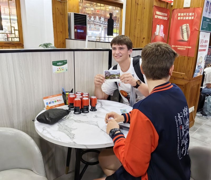 外國游客在西江千戶苗寨景區(qū)通過移動支付購買蓋有西江郵政郵戳的明信片。