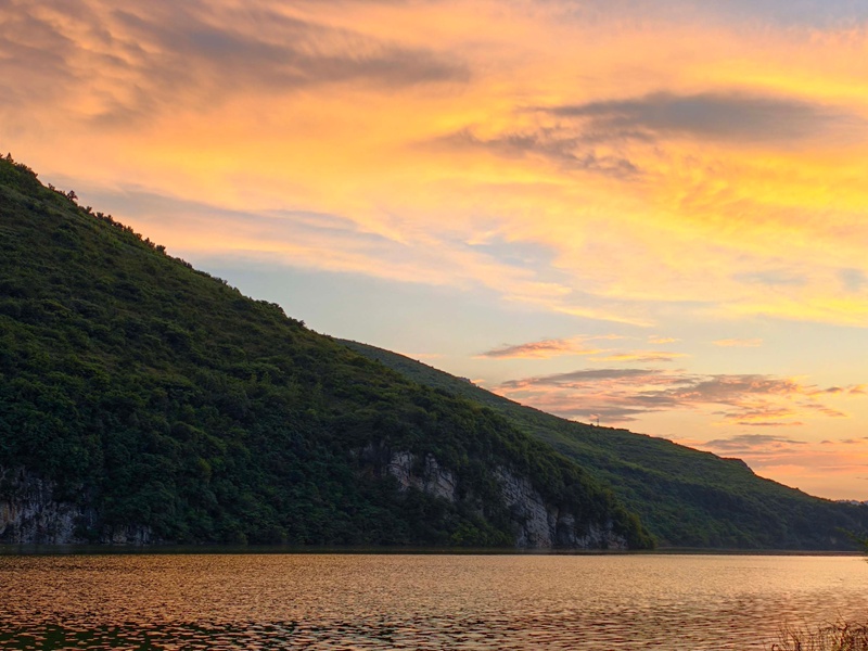 雨后的夾巖水庫空氣清新，落日余暉穿透云層，為天際染上橙紅、鎏金與淡紫的漸變色。張榮攝