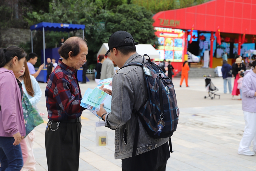 云巖區(qū)文體廣電旅游局工作人員正將《旅游安全實務(wù)手冊》遞到游客手中，準(zhǔn)備進行詳細講解。